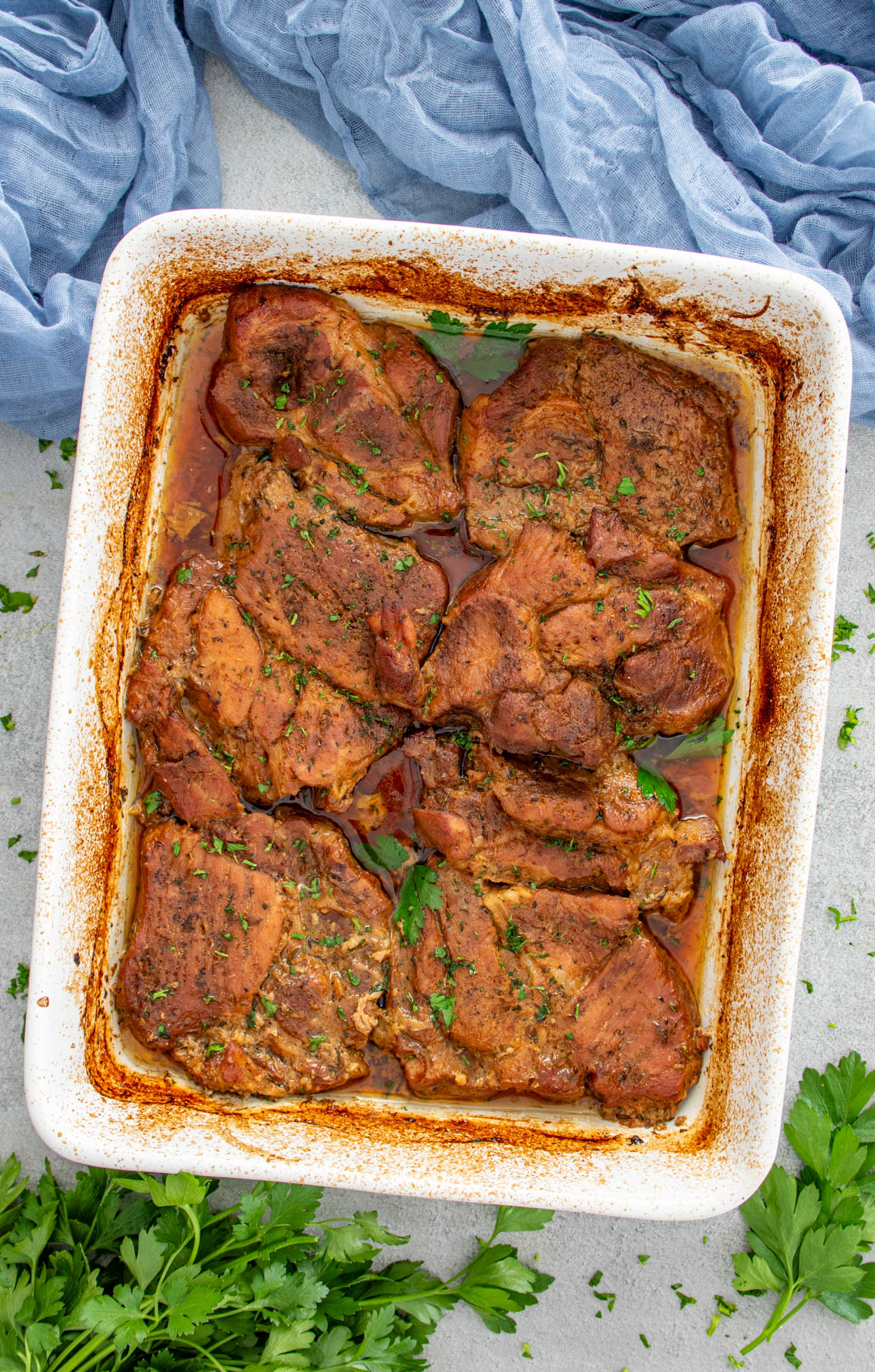 Ceafă de porc friptă la cuptor în tavă, suculentă și rumenită, presărată cu verdeață proaspătă.