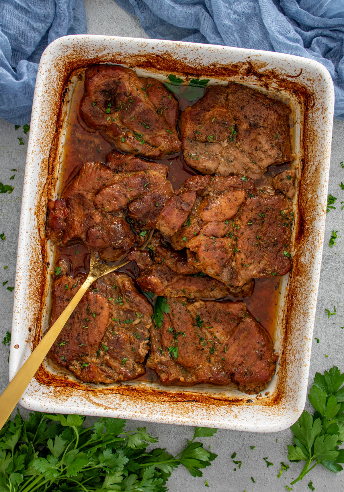 Ceafă de porc friptă la cuptor în tavă, suculentă și rumenită, presărată cu verdeață proaspătă.