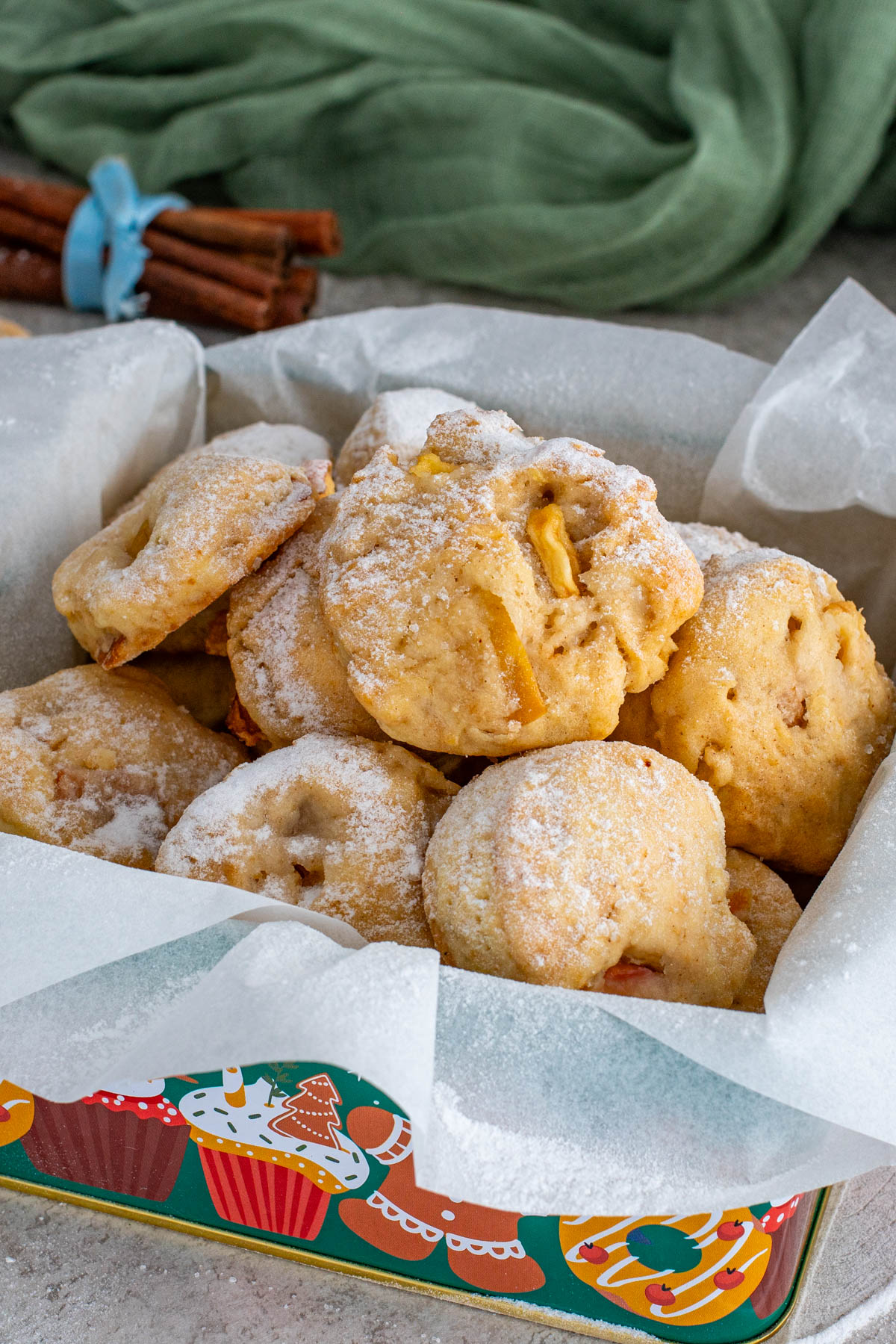 Biscuiți pufoși cu mere și scorțișoară, pudrați cu zahăr, așezați într-o cutie decorată de sărbători.