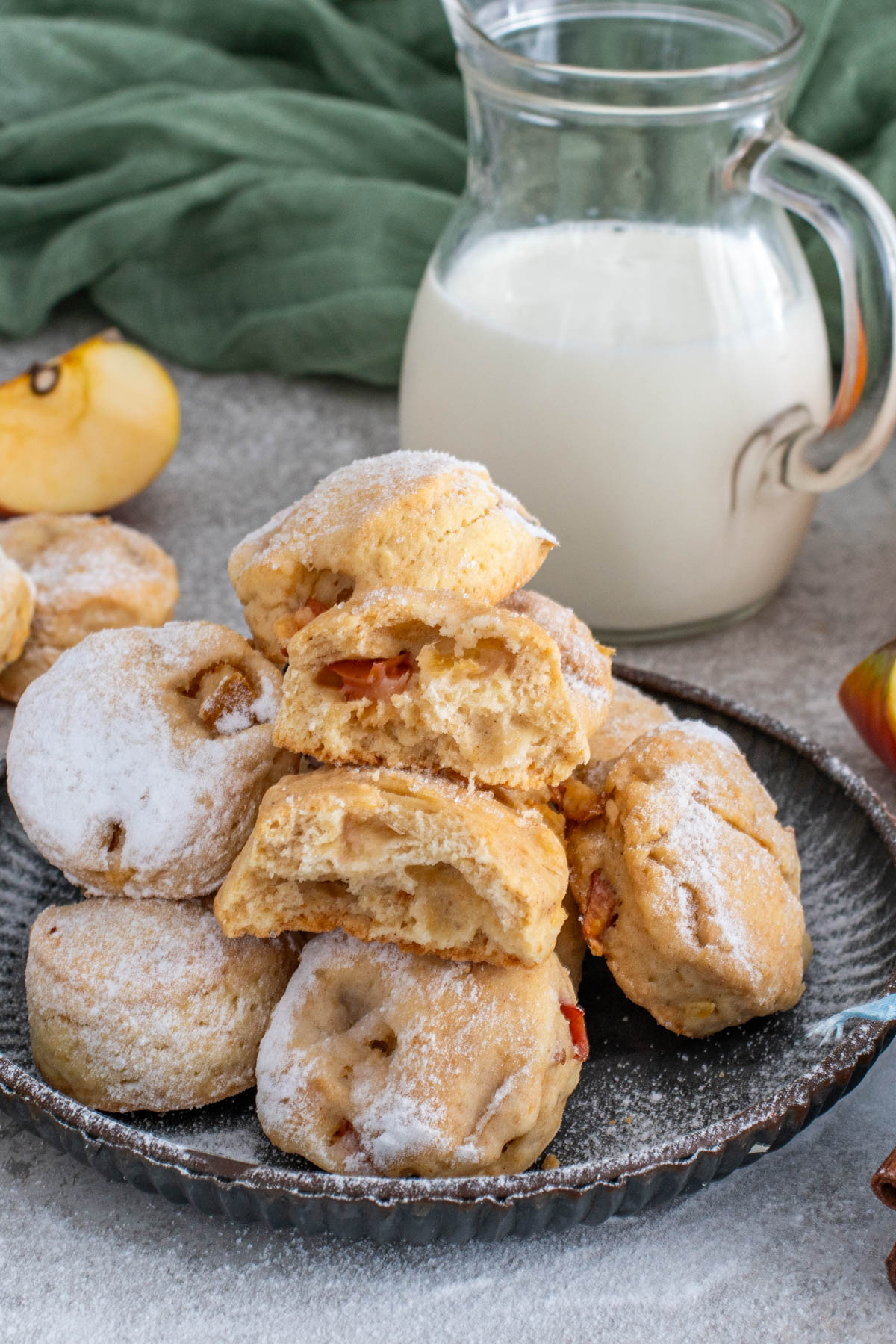 Biscuiți pufoși cu mere și scorțișoară, pudrați cu zahăr, așezați pe o farfurie, lângă un recipient cu lapte.