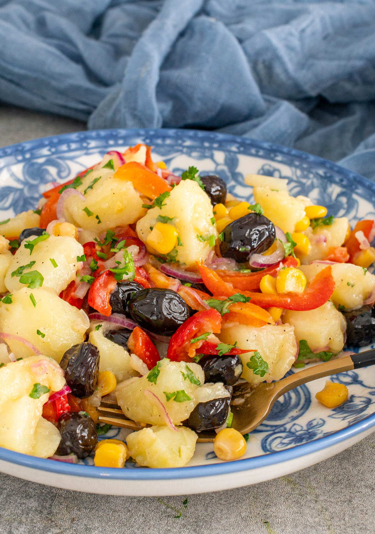 O porție de salată orientală de post, pregătită cu cartofi fierți, ceapă, măsline și castraveți murați, servită într-o farfurie și surprinsă în timp ce o furculiță ridică o parte din salată.