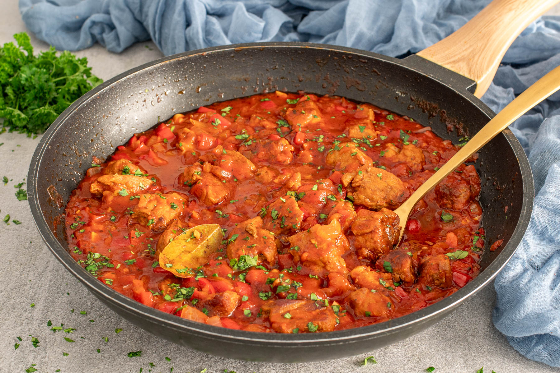 Tocană de porc în sos roșu cu ardei și ceapă, gătită într-o tigaie și presărată cu verdeață proaspătă.