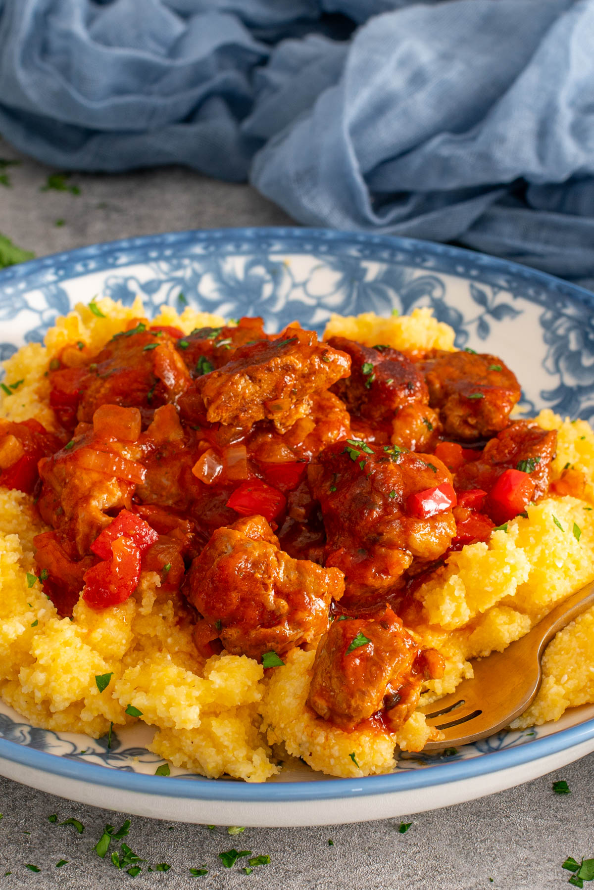 Tocană de porc cu sos roșu și legume, servită peste mămăligă pe o farfurie decorată.