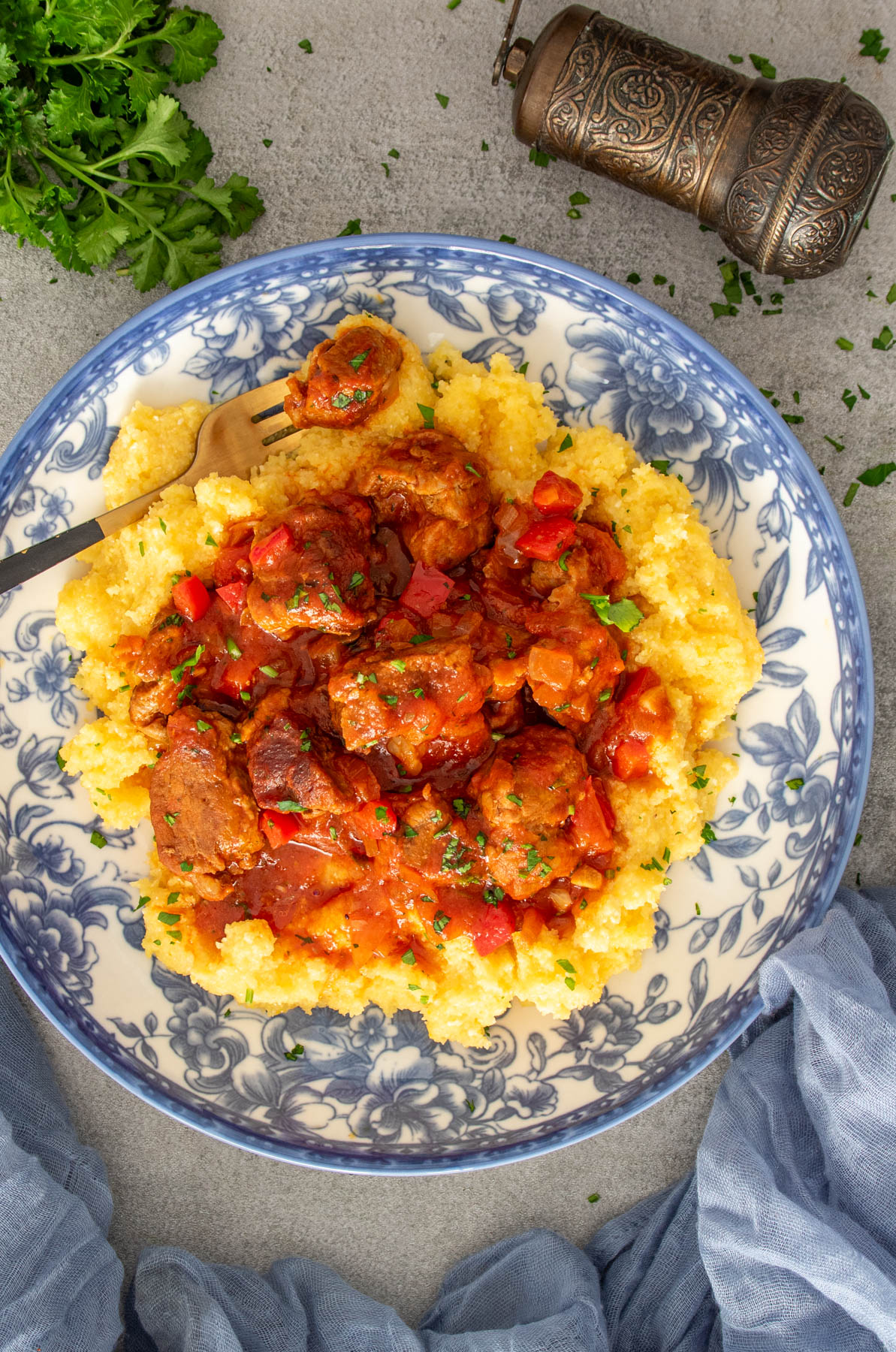 Tocană de porc cu ardei și ceapă, servită peste un pat de mămăligă pufoasă, în farfurie decorată cu model floral.