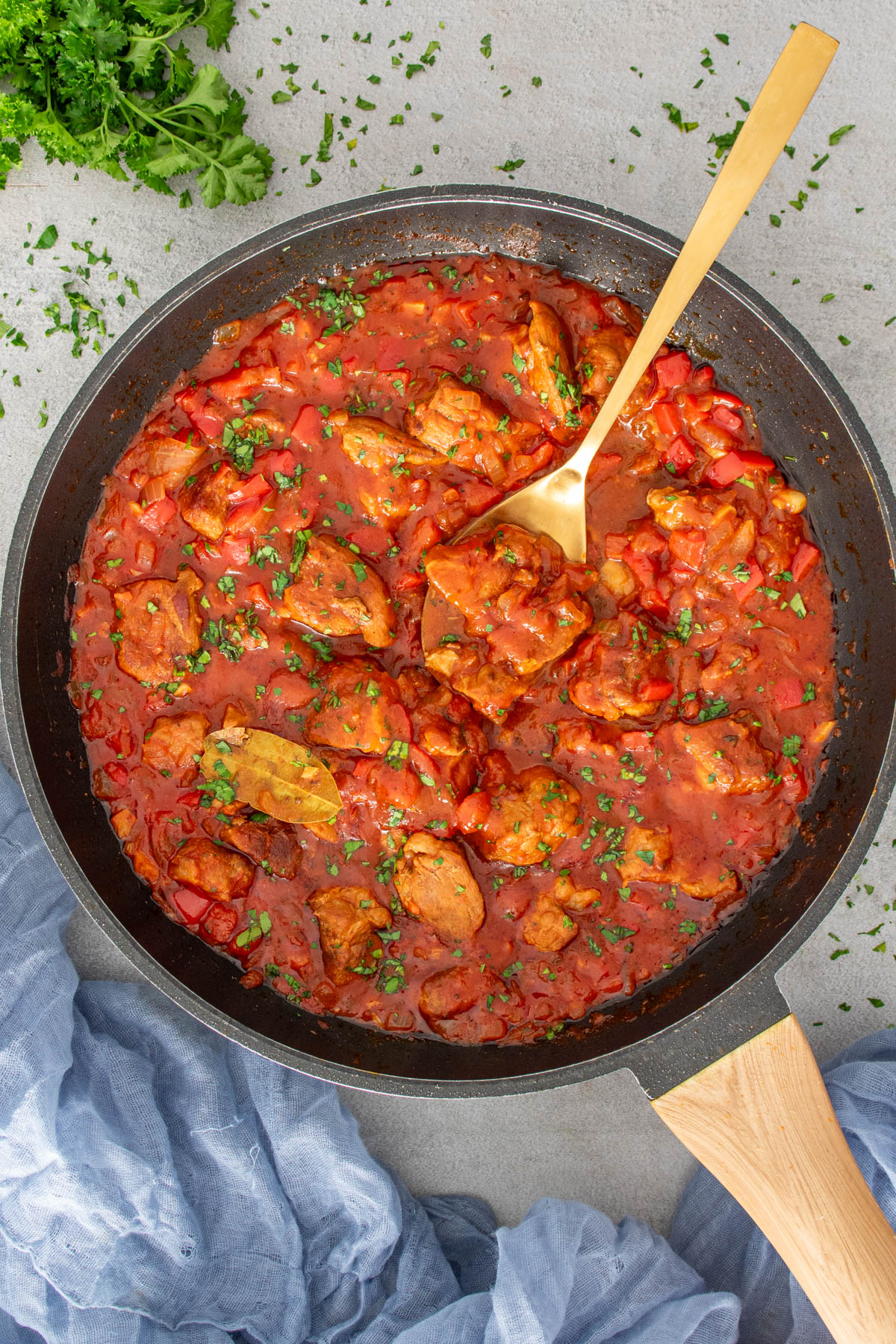 Tocană de porc în sos roșu cu ardei și ceapă, gătită într-o tigaie și presărată cu verdeață proaspătă.