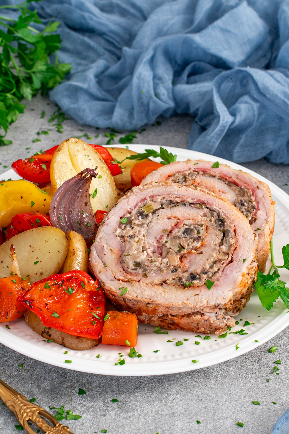 Felii de rulada de porc cu ciuperci, servite cu legume caramelizate la cuptor.