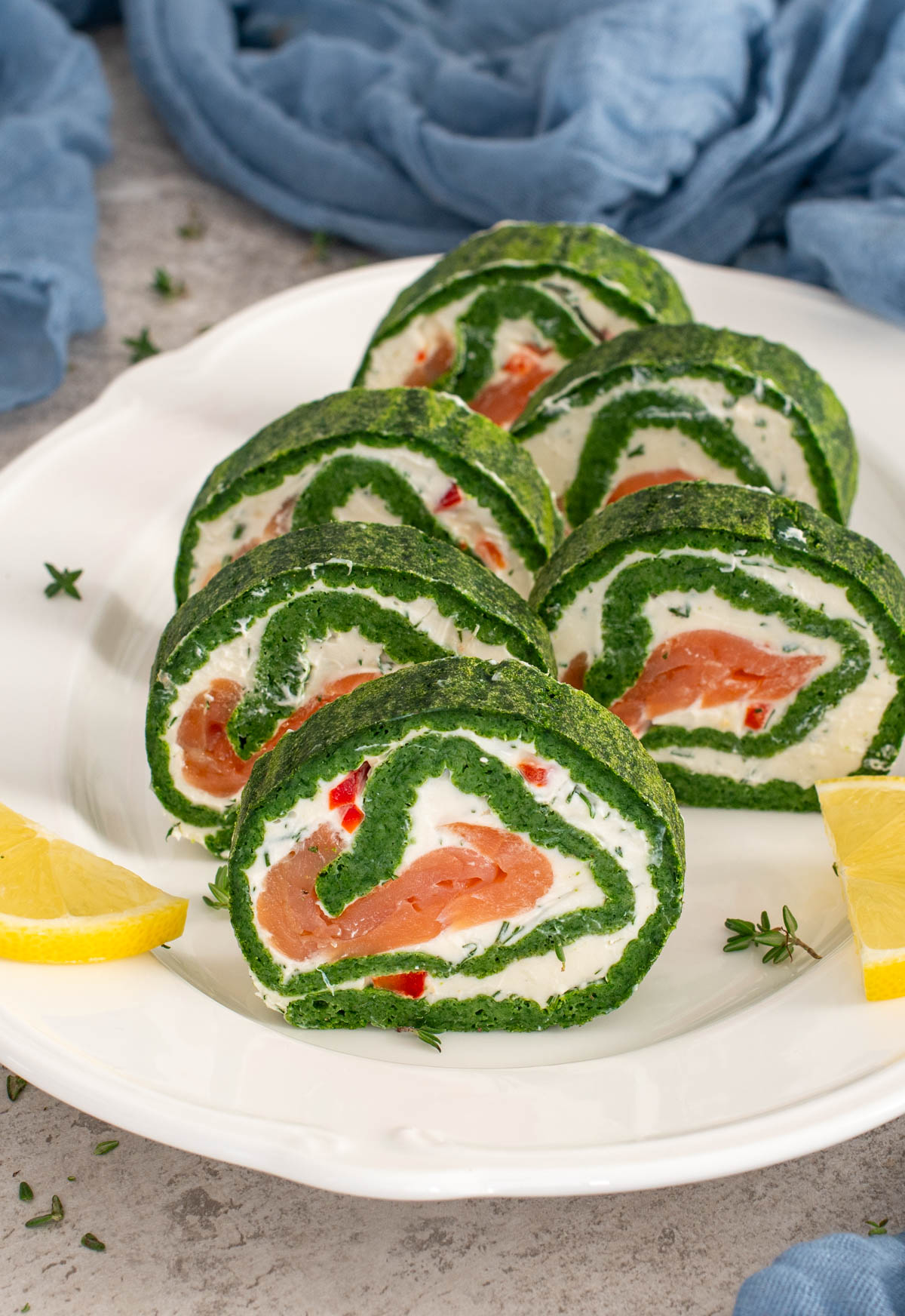 Ruladă aperitiv din spanac, tăiată felii, cu umplutură de cremă de br&acirc;nză, somon afumat și ardei, servită cu lăm&acirc;ie.