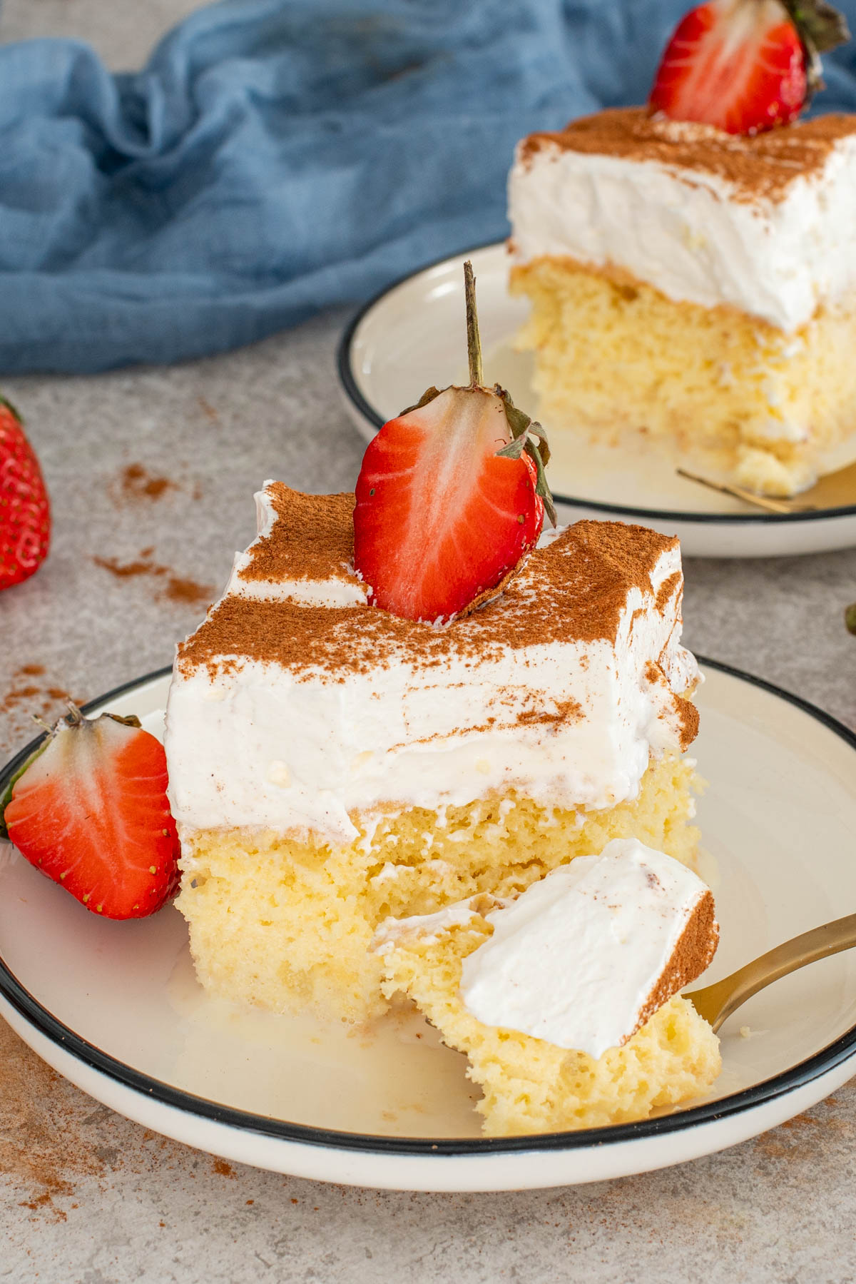 Prăjitură Tres Leches servită la farfurie, cu blat &icirc;nsiropat, frișcă aerată, scorțișoară și căpșuni.