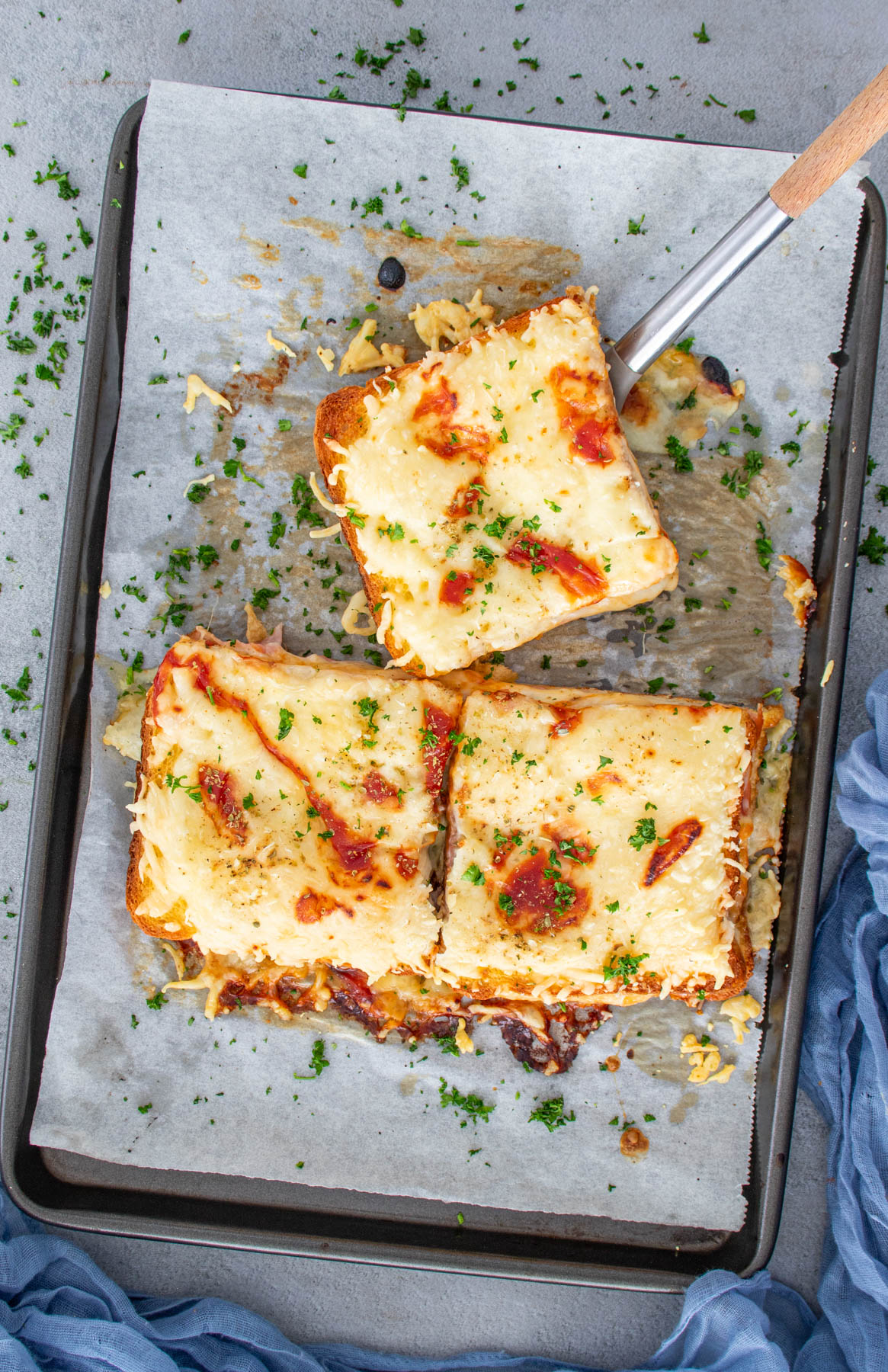 Sendvișuri gratinate cu p&acirc;ine șuncă, mozzarella si cascaval, asezonate cu patrunjel.