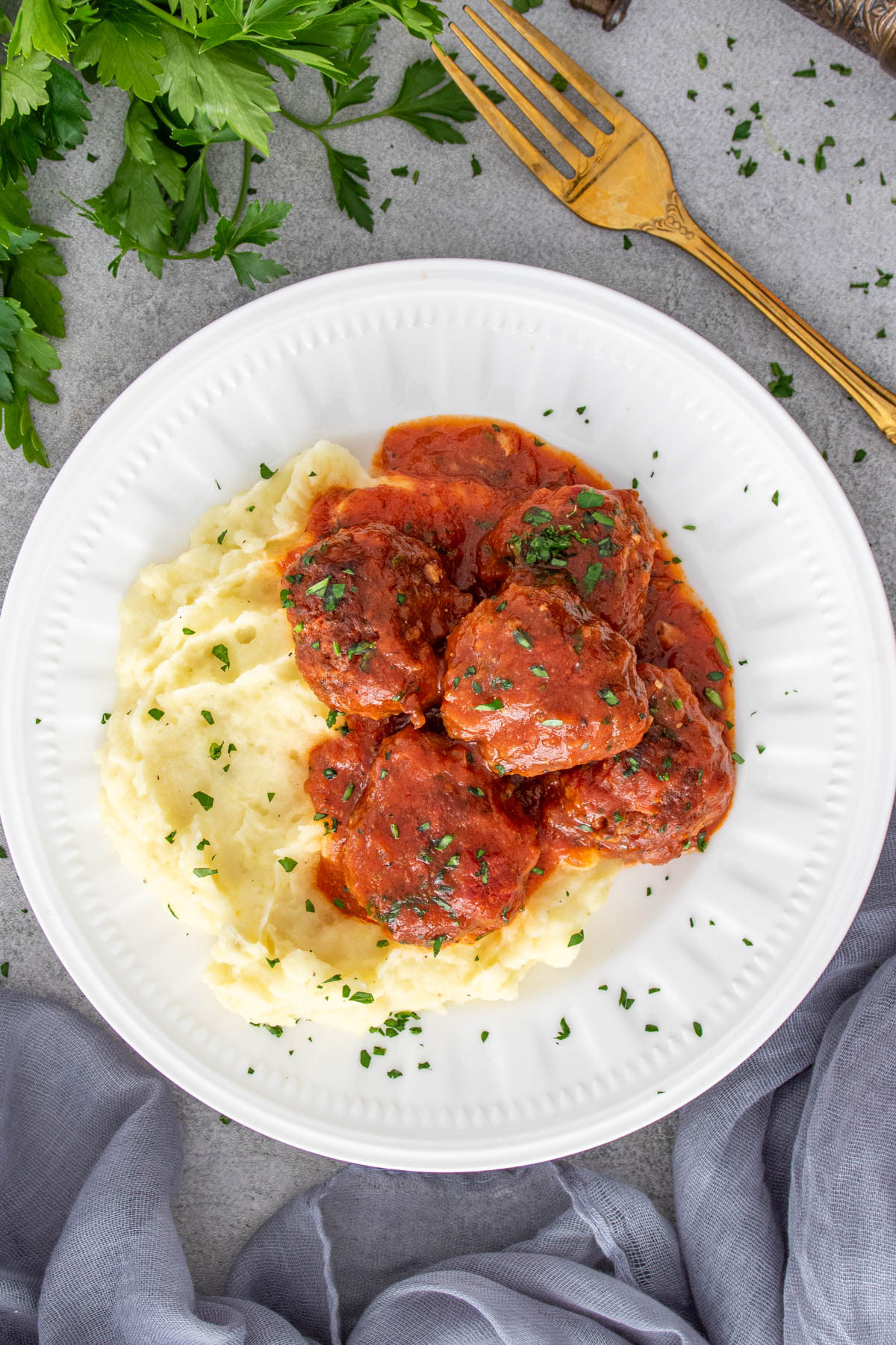 Chifteluțe marinate &icirc;n sos de roșii cu piure de cartofi, servite pe farfurie.