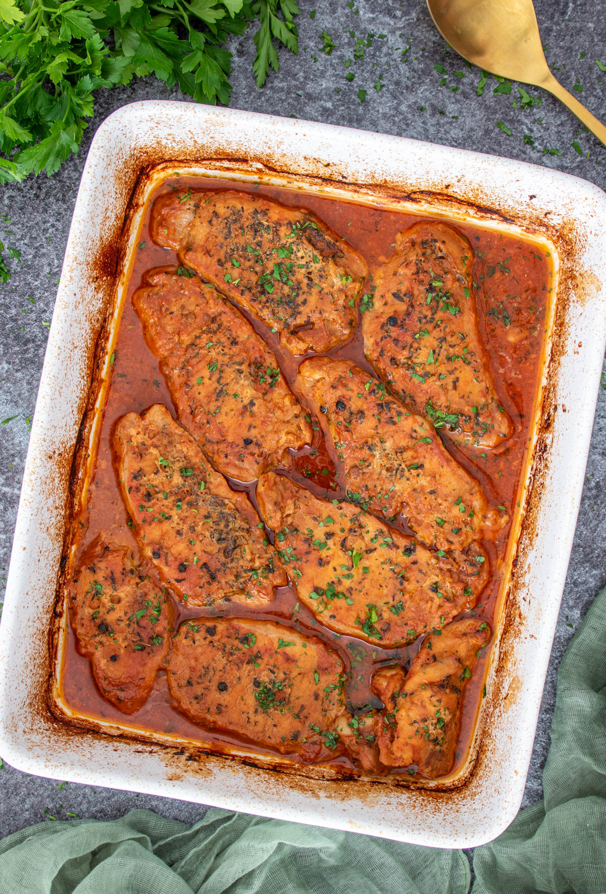 Tava scoasa din cuptor cu cotlete rumenite cu sos rosu si usturoi.