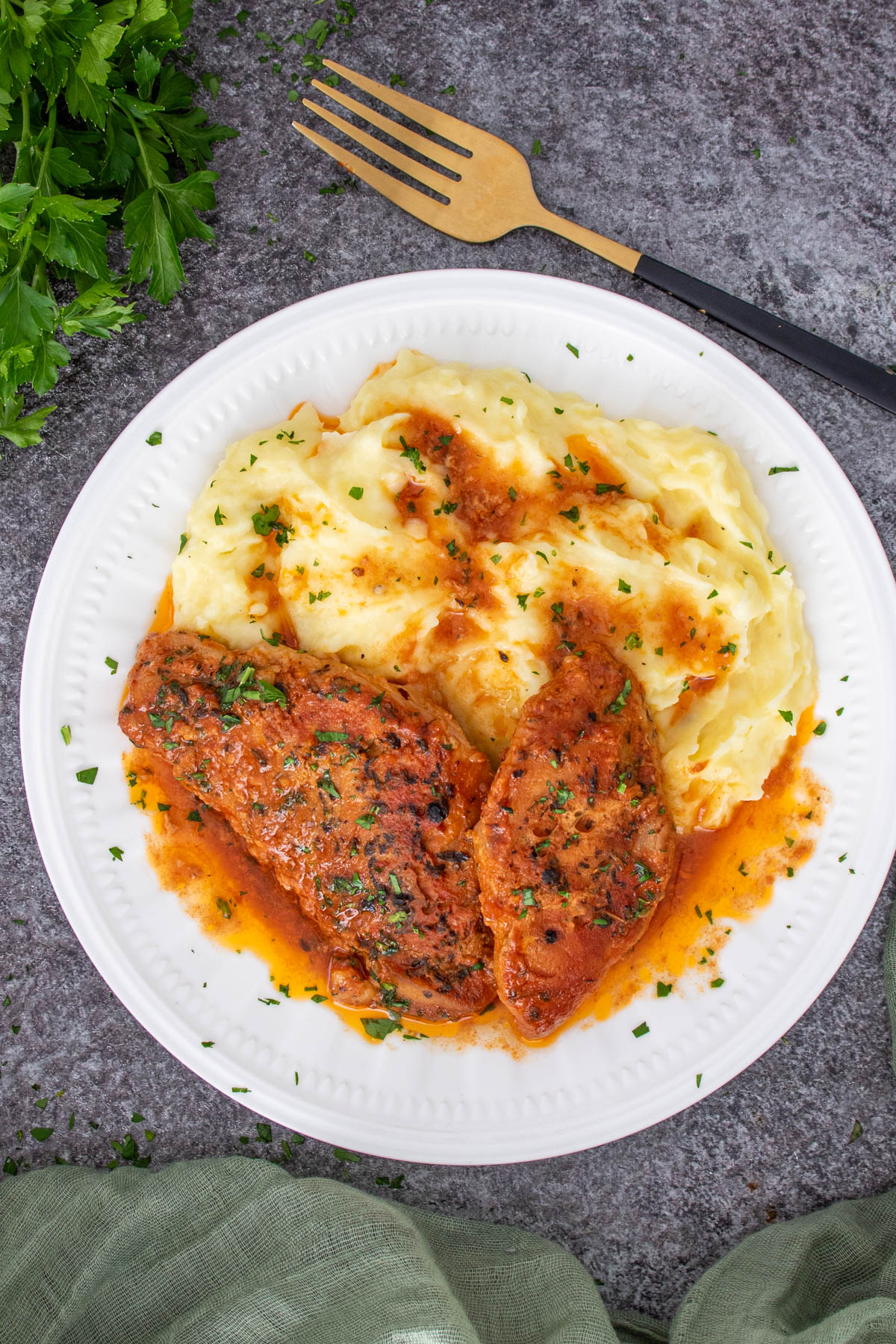 Cotlete de porc cu sos rosu si usturoi, servite pe o farfurie alba alaturi de o garnitura de piure.