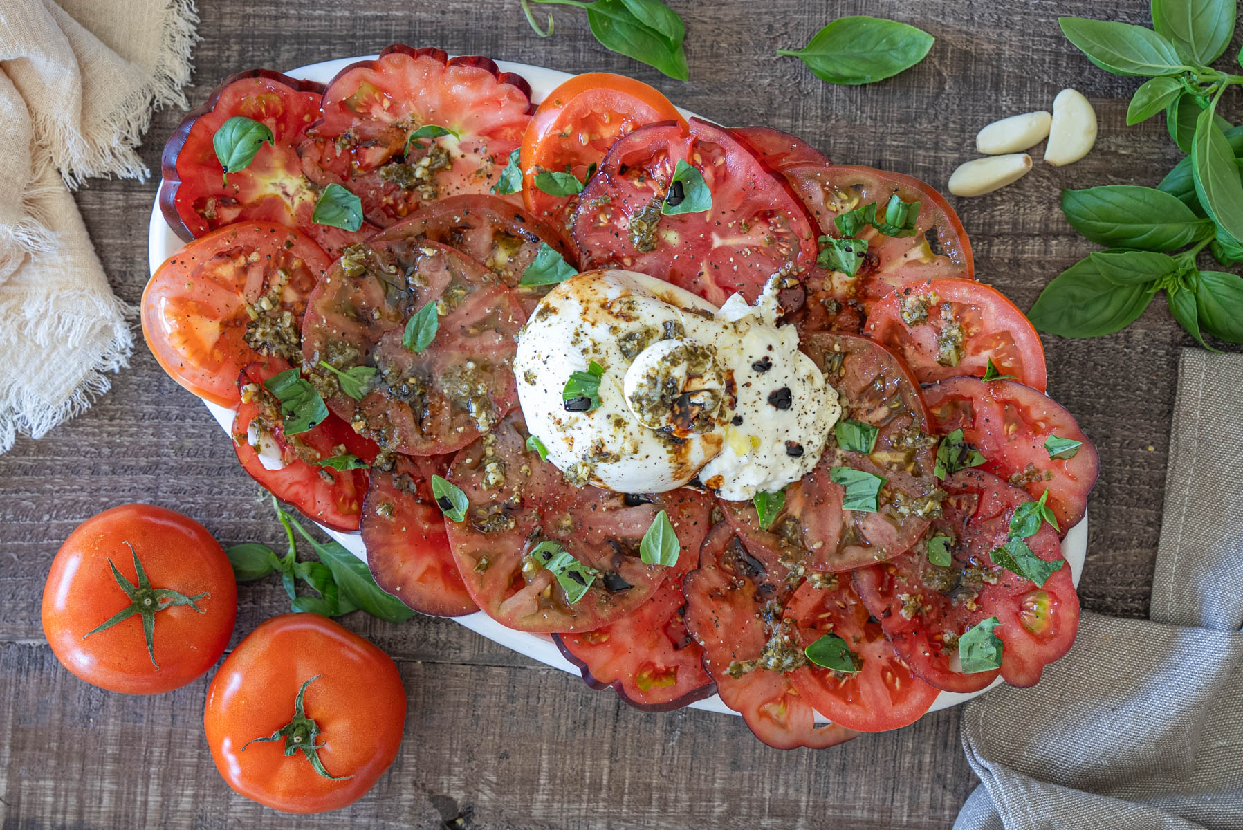 Salată cu burrata cremoasă, roșii de grădină feliate, pesto de busuioc și frunze proaspete de busuioc, servită pe un platou rustic.