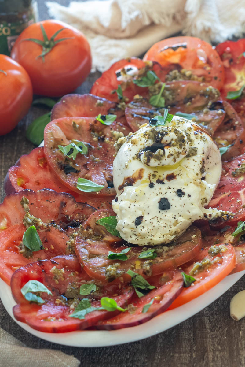 Salată cu burrata cremoasă, roșii proaspete, pesto de busuioc și reducție balsamică, servită pe un platou alb.