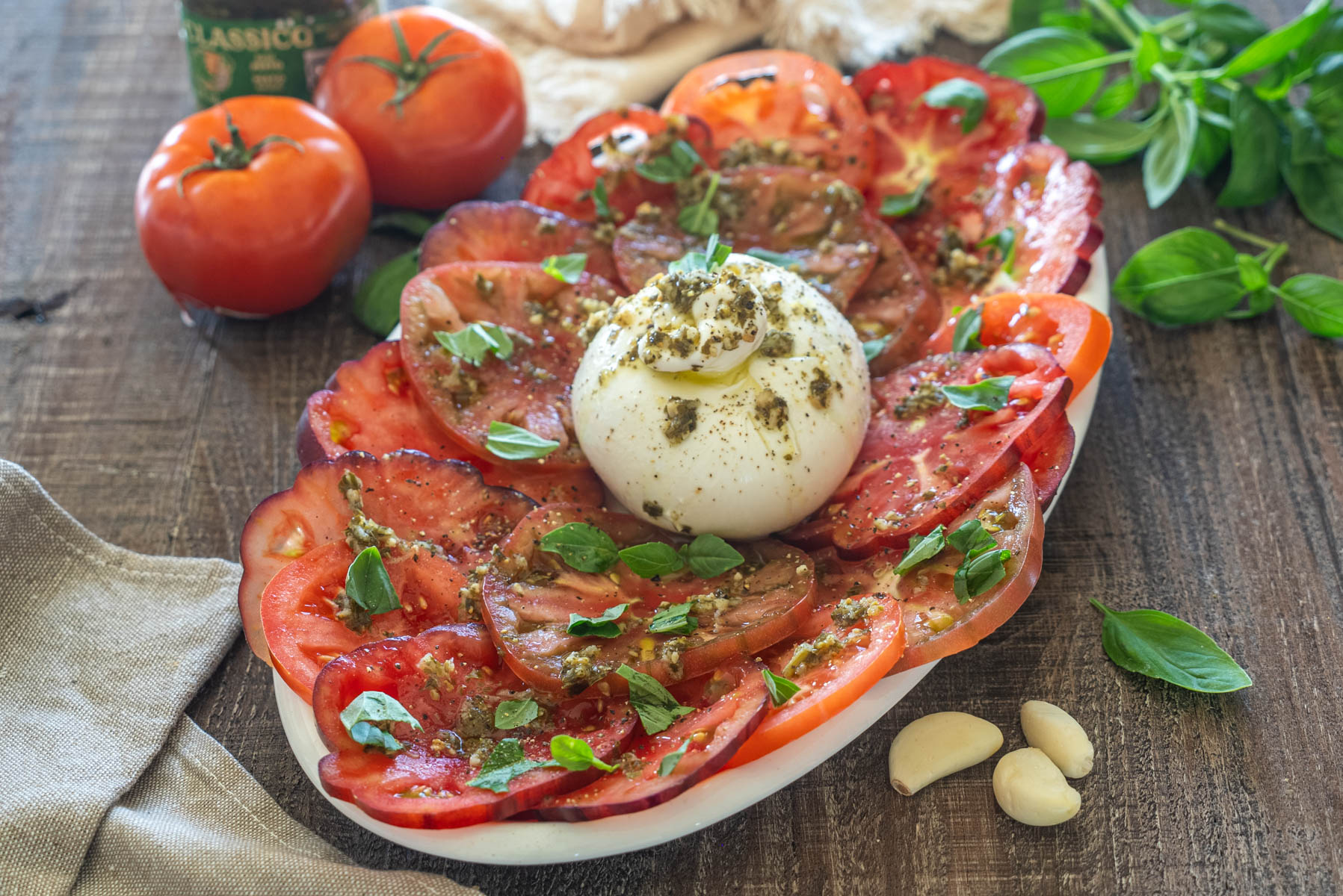 Salată cu burrata cremoasă, roșii de grădină feliate, pesto de busuioc și frunze proaspete de busuioc, servită pe un platou rustic.