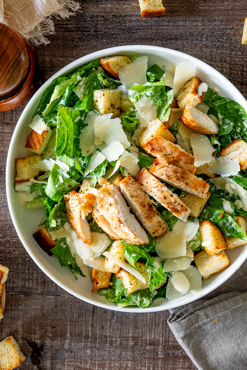 Salată Caesar cu piept de pui la grătar, salată romaine, crutoane crocante, fulgi de parmezan și dressing Caesar, fotografiată de sus.