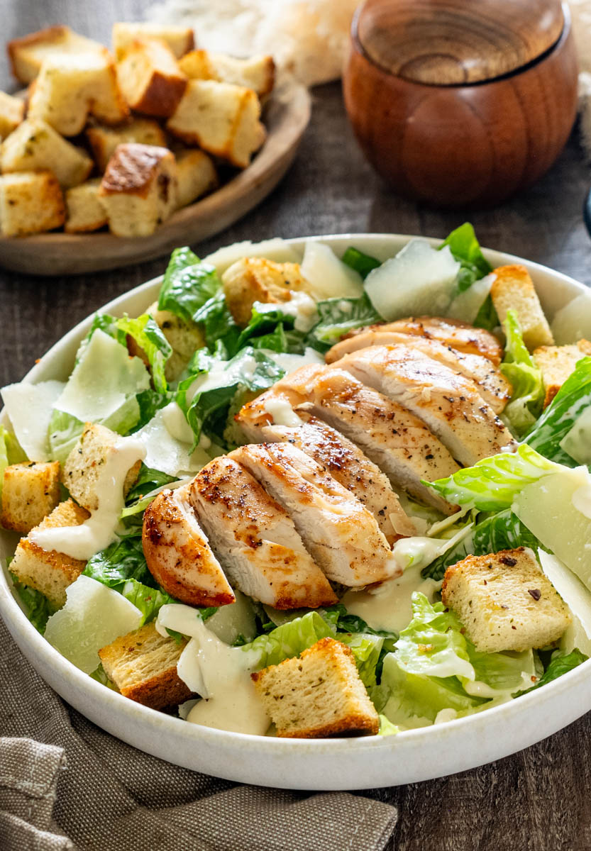 Salată Caesar cu piept de pui la grătar, salată romaine, crutoane crocante, fulgi de parmezan și dressing Caesar, servită într-un bol.