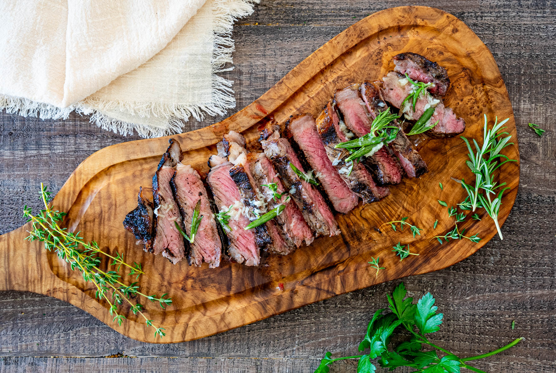 Steak de vită la grătar cu unt aromatizat, rozmarin și cimbru, servit pe un platou rustic.