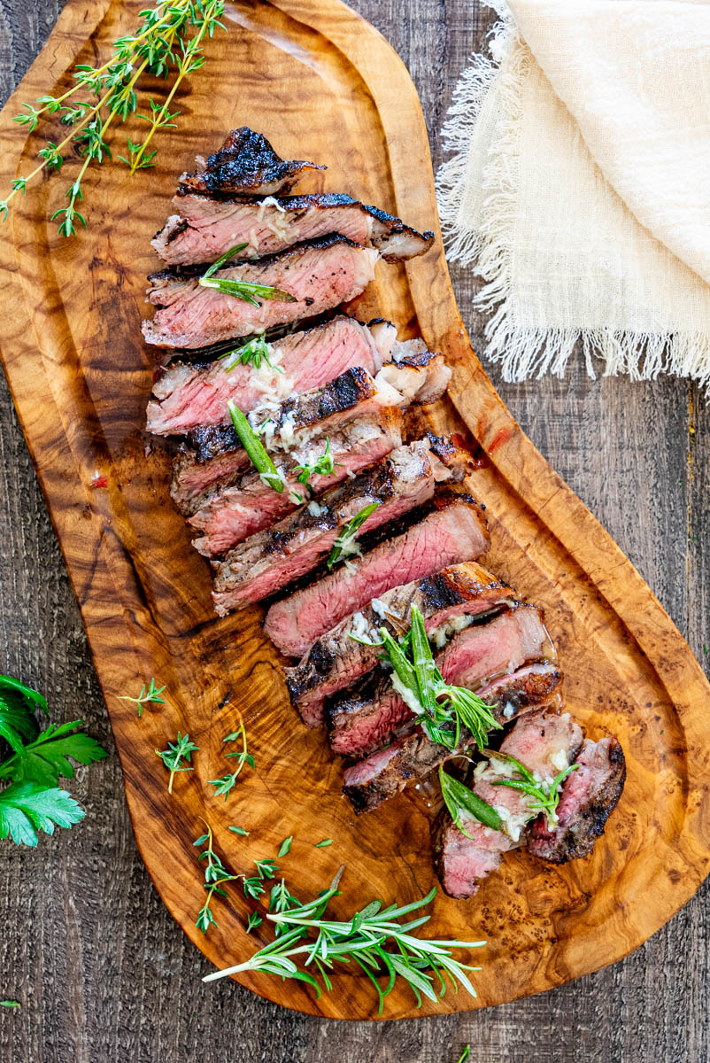 Steak canadian la grătar, fraged și suculent, feliat și servit pe un tocător din lemn.