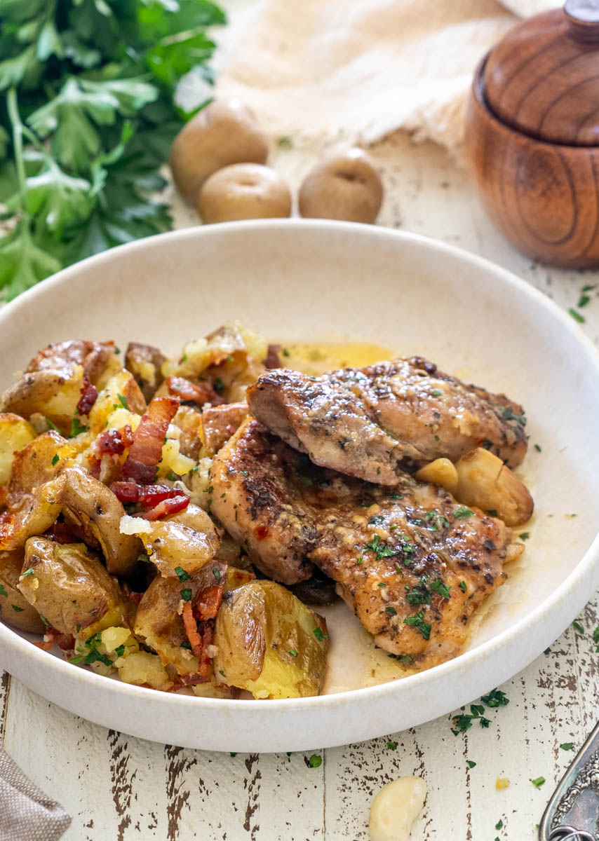 Pulpe de pui rumenite și cartofi copți cu bacon, un preparat gustos pentru prânz sau cină.