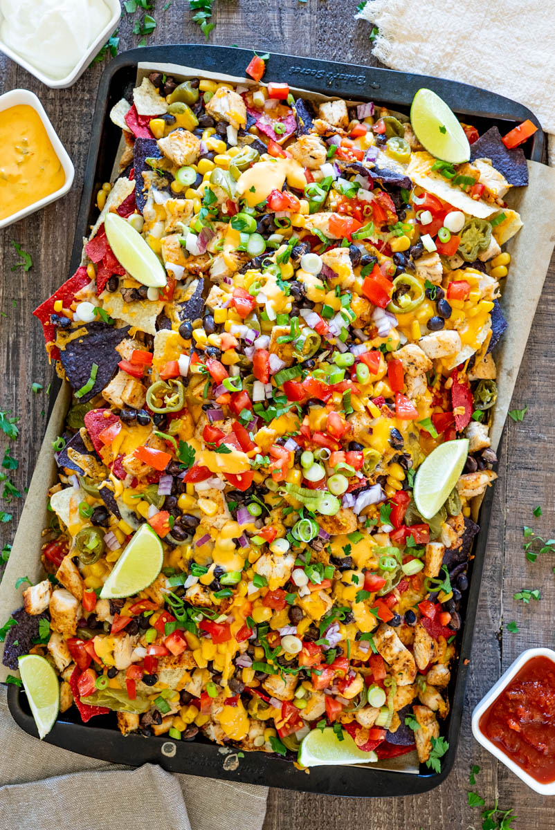 Nachos cu pui și br&acirc;nză topită, serviți cu porumb, fasole neagră, roșii, jalape&ntilde;o, ceapă verde și lime.