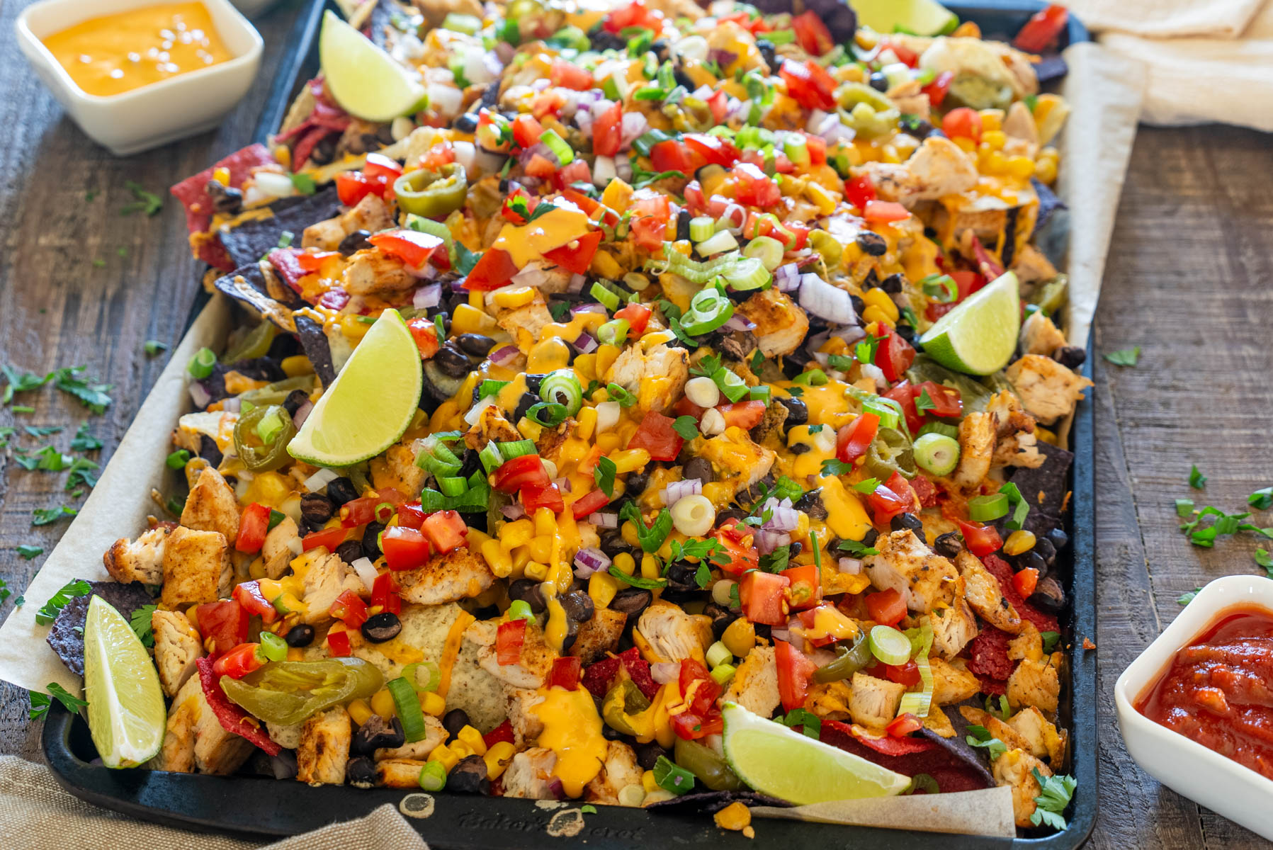 Nachos cu pui la tavă, &icirc;ncărcați cu cheddar topit, porumb, fasole neagră, jalape&ntilde;o, roșii și ceapă verde.