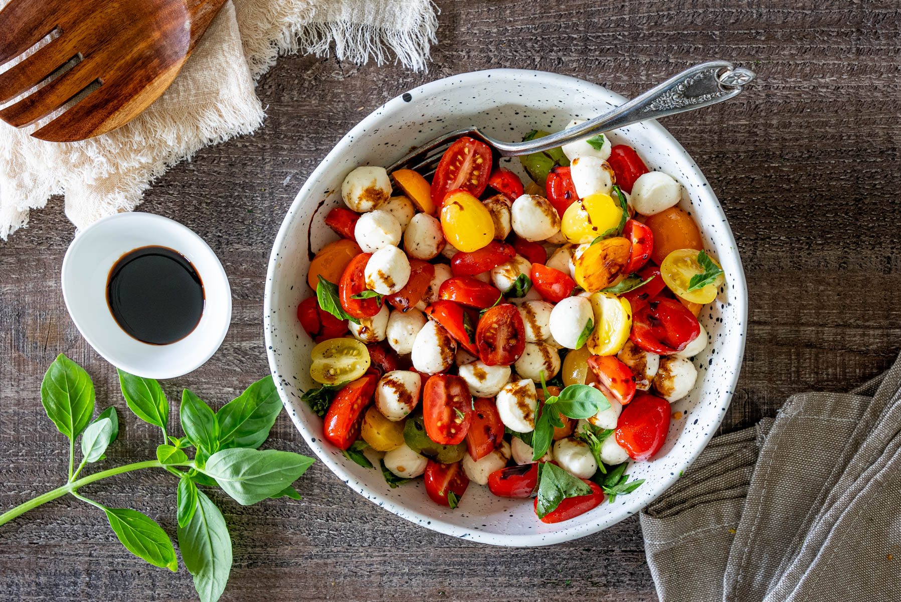 Salată Caprese cu roșii cherry multicolore, mini mozzarella, frunze proaspete de busuioc și glazură de oțet balsamic, servită într-un bol.