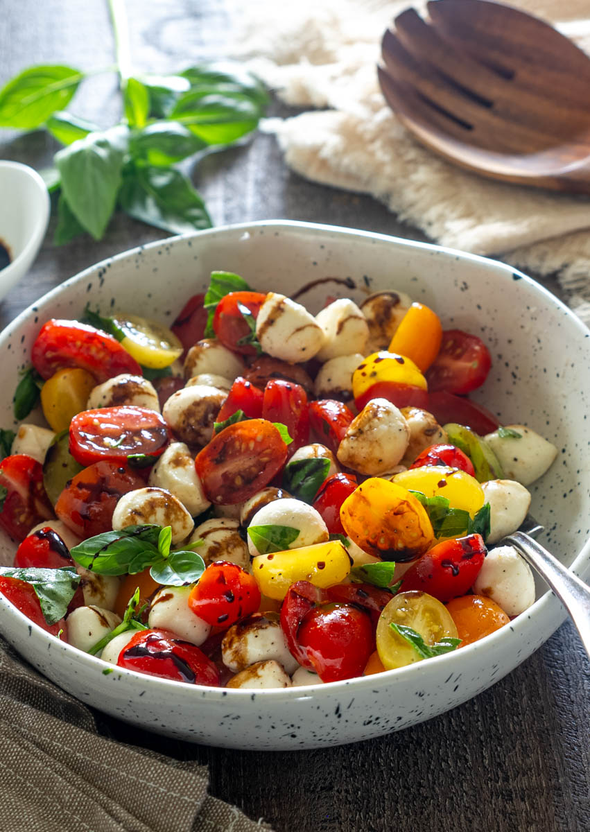alată Caprese cu roșii cherry multicolore, mini mozzarella, busuioc proaspăt și glazură de oțet balsamic, servită într-un bol ceramic.