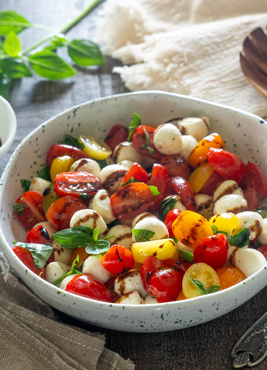 Salată Caprese cu roșii cherry multicolore, mini mozzarella, busuioc proaspăt și glazură de oțet balsamic, servită într-un bol ceramic.