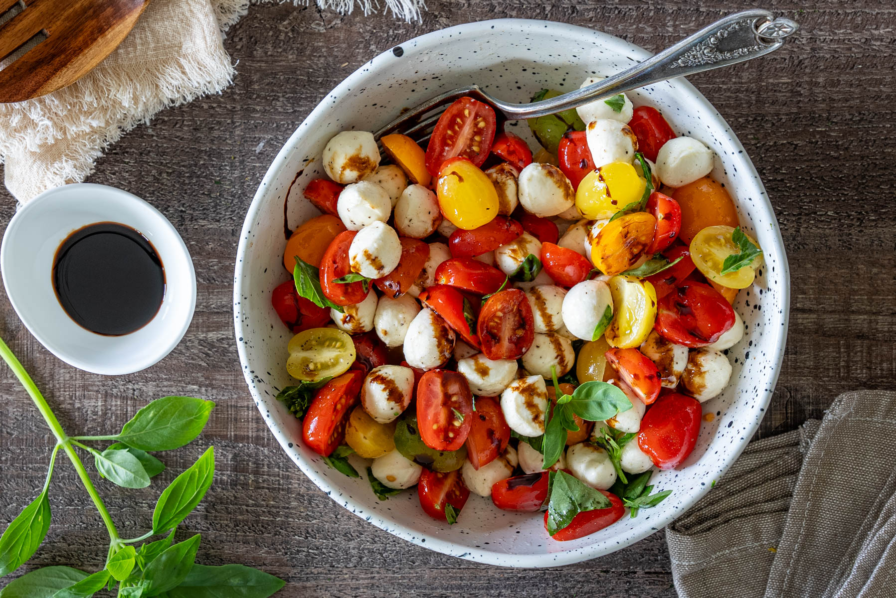 Salată Caprese cu roșii cherry multicolore, mini mozzarella, frunze proaspete de busuioc și glazură de oțet balsamic, servită într-un bol.