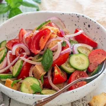Salată Panzanella cu roșii, castraveți, ceapă roșie, bucăți de pâine și busuioc, într-un bol alb.