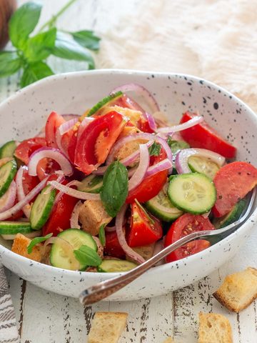 Salată Panzanella cu roșii, castraveți, ceapă roșie, bucăți de p&acirc;ine și busuioc, &icirc;ntr-un bol alb.