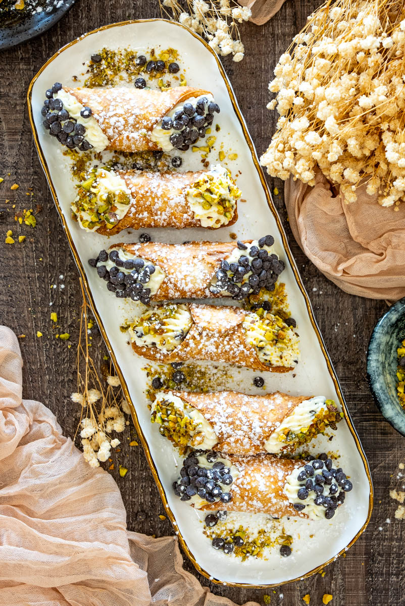 Platou cu cannoli de casă, pudrați cu zahăr și umpluți cu cremă, fistic mărunțit și chipsuri de ciocolată.