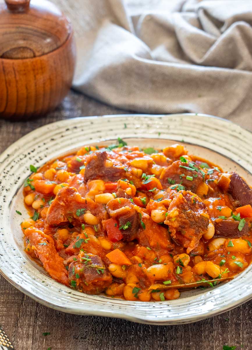 Porție de iahnie de fasole cu ciolan afumat, fasole albă și legume.