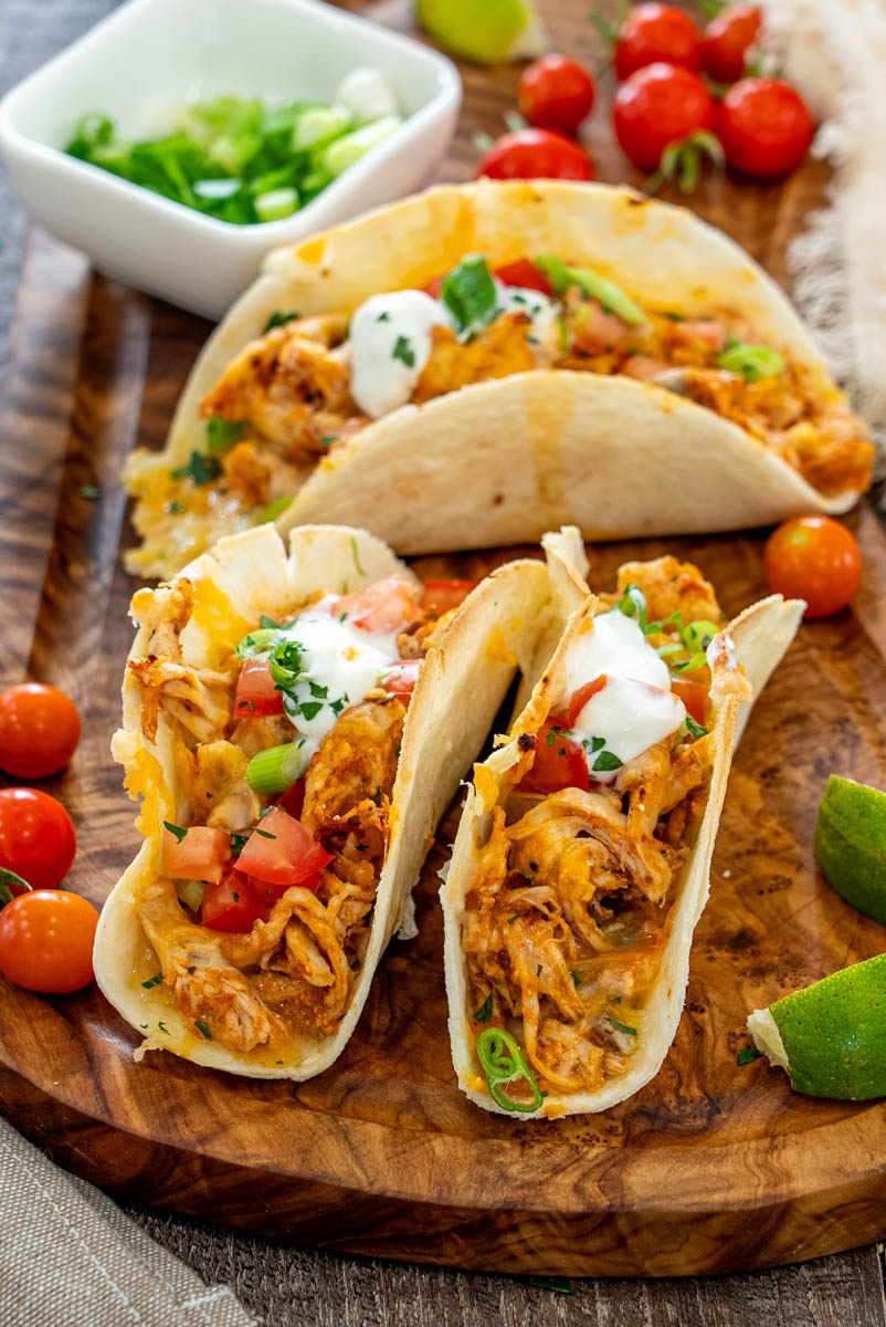 Tacos cu pui, br&acirc;nză topită, roșii, ceapă verde și sos cremos, serviți &icirc;n tortilla rumenită.