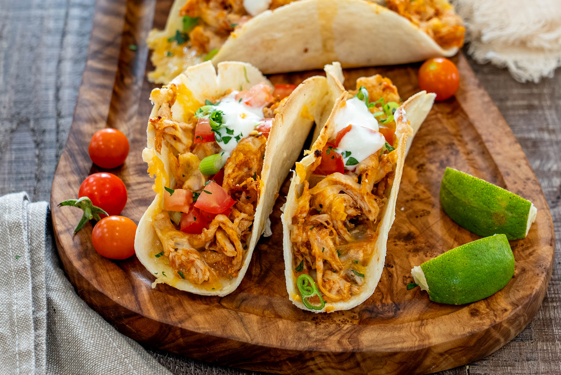 Tacos cu pui fraged și br&acirc;nză topită, garnisiți cu roșii proaspete, ceapă verde și sos cremos, serviți alături de lime.