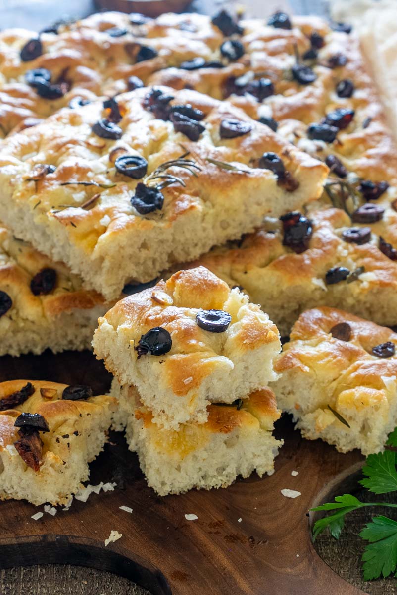 Focaccia pufoasă cu măsline negre, rozmarin și usturoi, tăiată în bucăți.