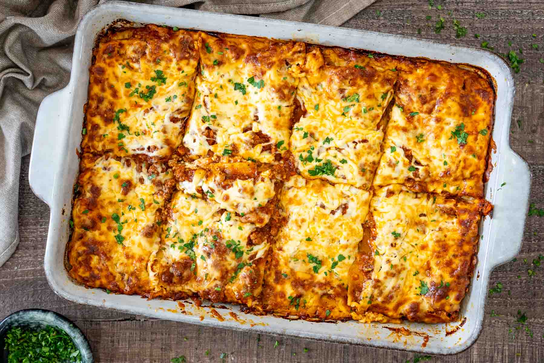 Lasagna cu carne și ricotta la cuptor, acoperită cu mozzarella și parmezan rumenite și presărată cu pătrunjel proaspăt.