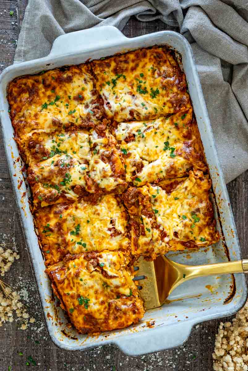 Lasagna cu carne și ricotta rumenită la cuptor, cu mozzarella topită și o porție gata de servire.
