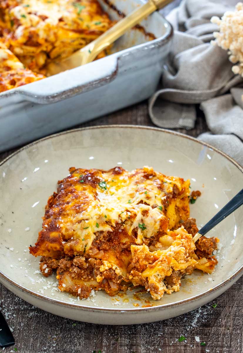 Lasagna cu carne tocată, sos de roșii, ricotta și mozzarella, rumenită la cuptor și servită în farfurie.