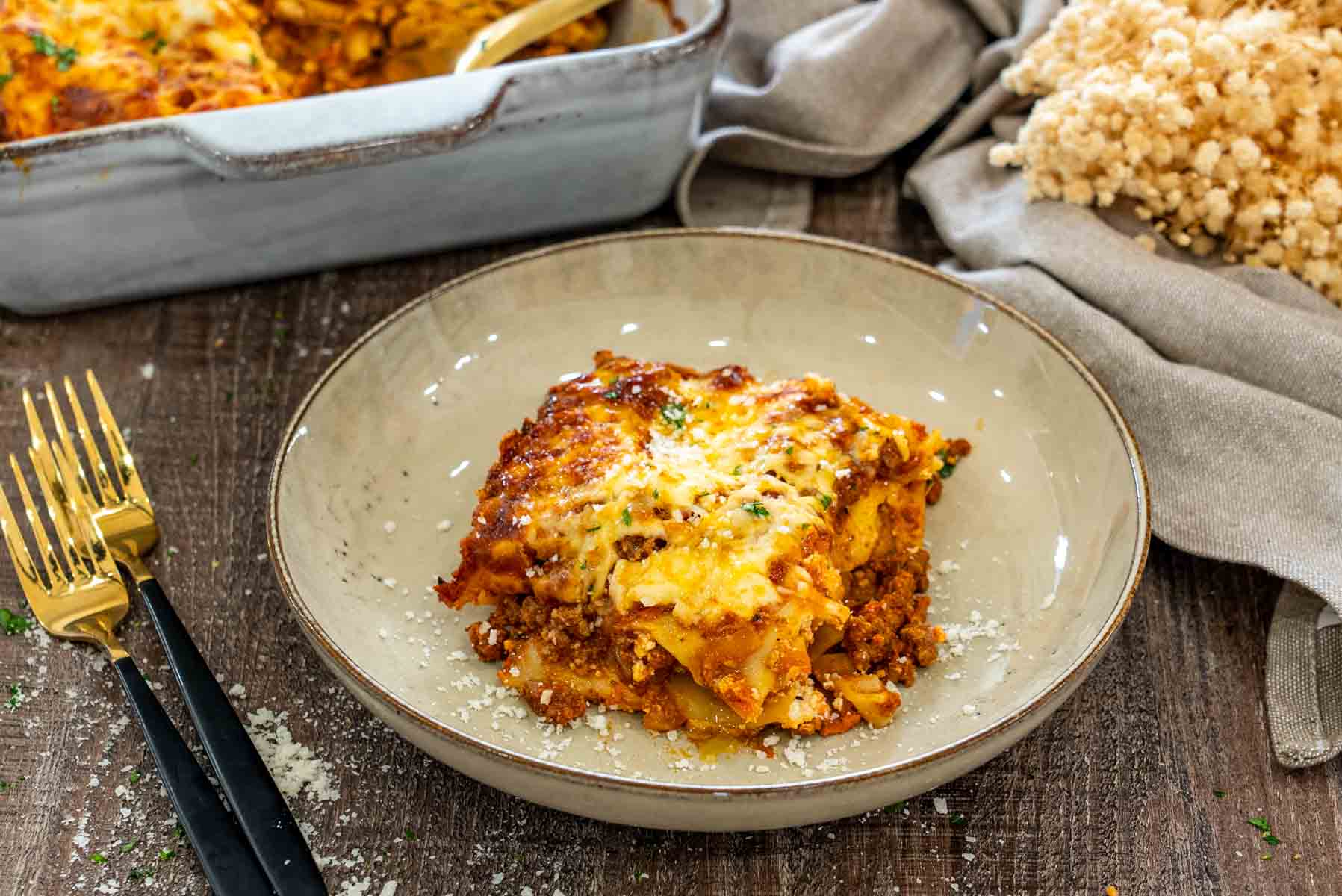 Porție de lasagna cu carne și ricotta, servită cu parmezan ras, cu straturi de paste, sos de carne și mozzarella rumenită.