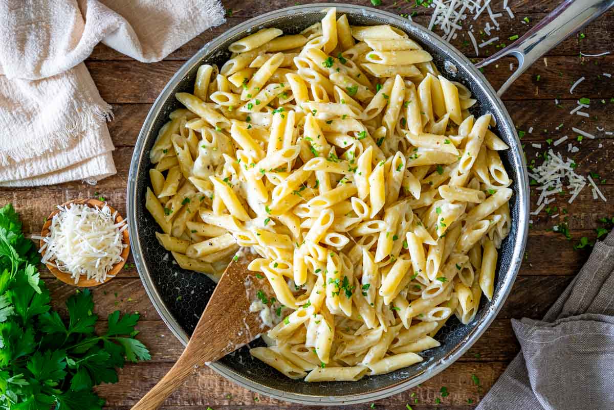 Tigaie cu paste penne Quattro Formaggi în sos cremos, presărate cu pătrunjel și piper.