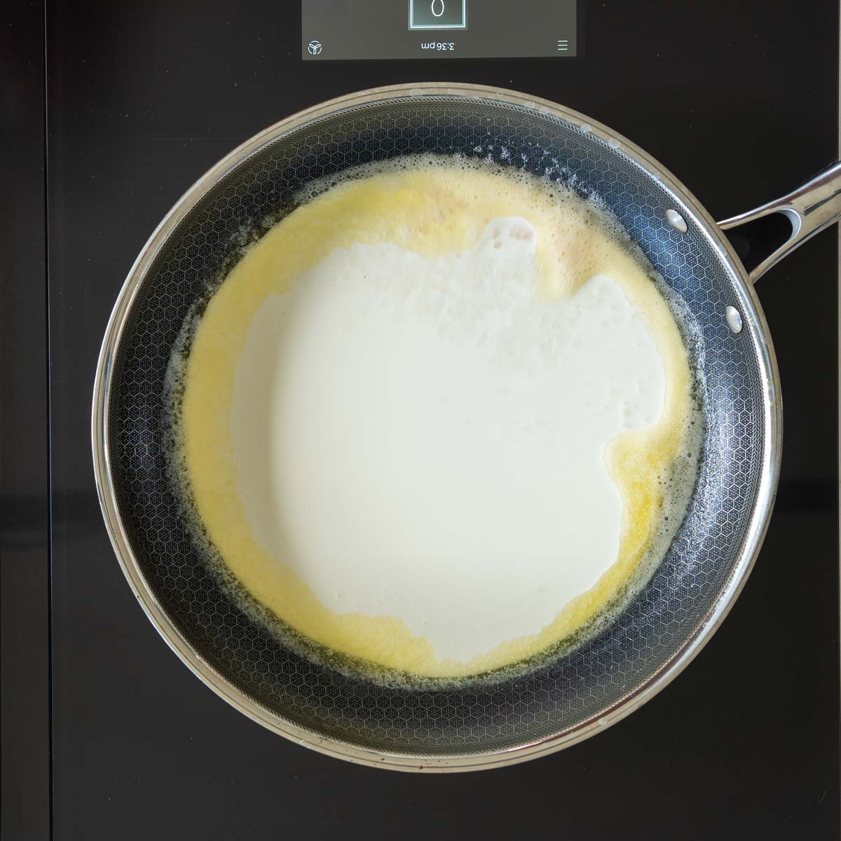Smântână lichidă turnată peste unt topit în tigaie pentru sosul Quattro Formaggi.