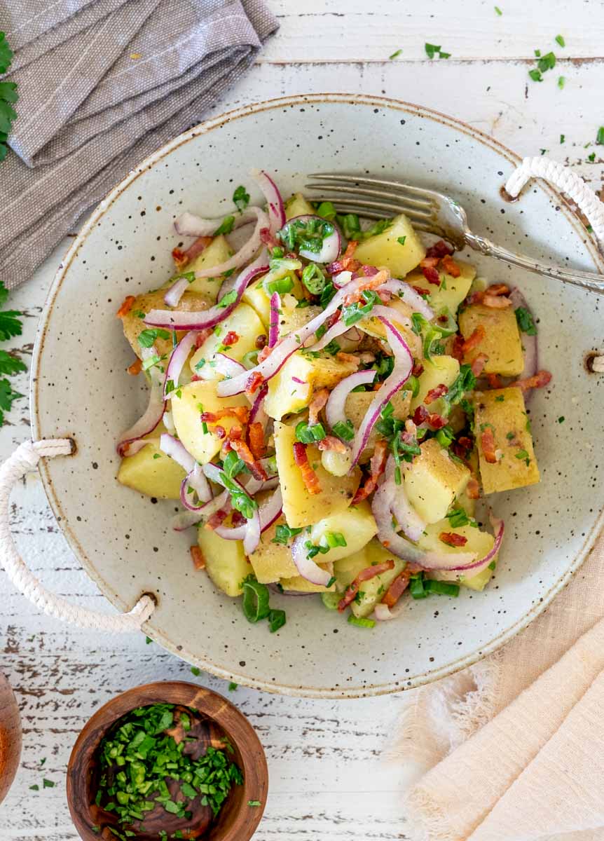 Porție de salată germană de cartofi cu bacon, ceapă roșie și verdeață.