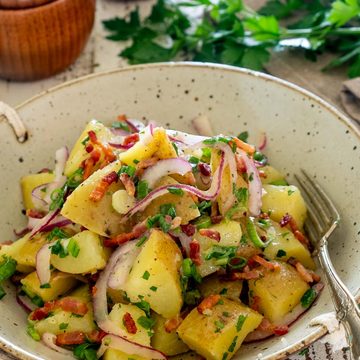 Salată germană de cartofi cu bacon crocant, ceapă roșie și verdeață.