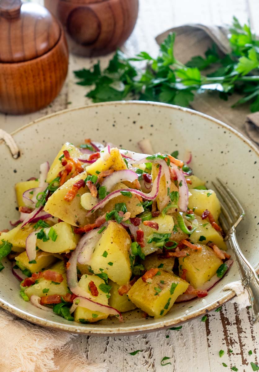 Salată germană de cartofi cu bacon crocant, ceapă roșie și verdeață.