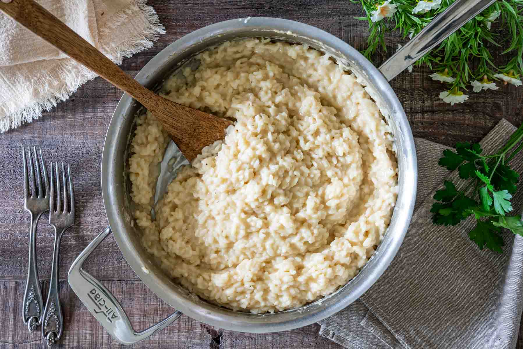 Risotto cremos cu parmezan într-o tigaie din inox, cu o spatulă de lemn, fotografiat de sus.