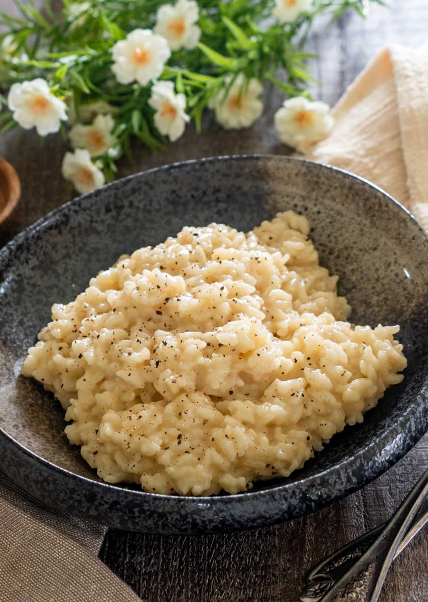 Risotto cremos cu parmezan, presărat cu piper negru, servit într-un bol gri pe o masă din lemn.