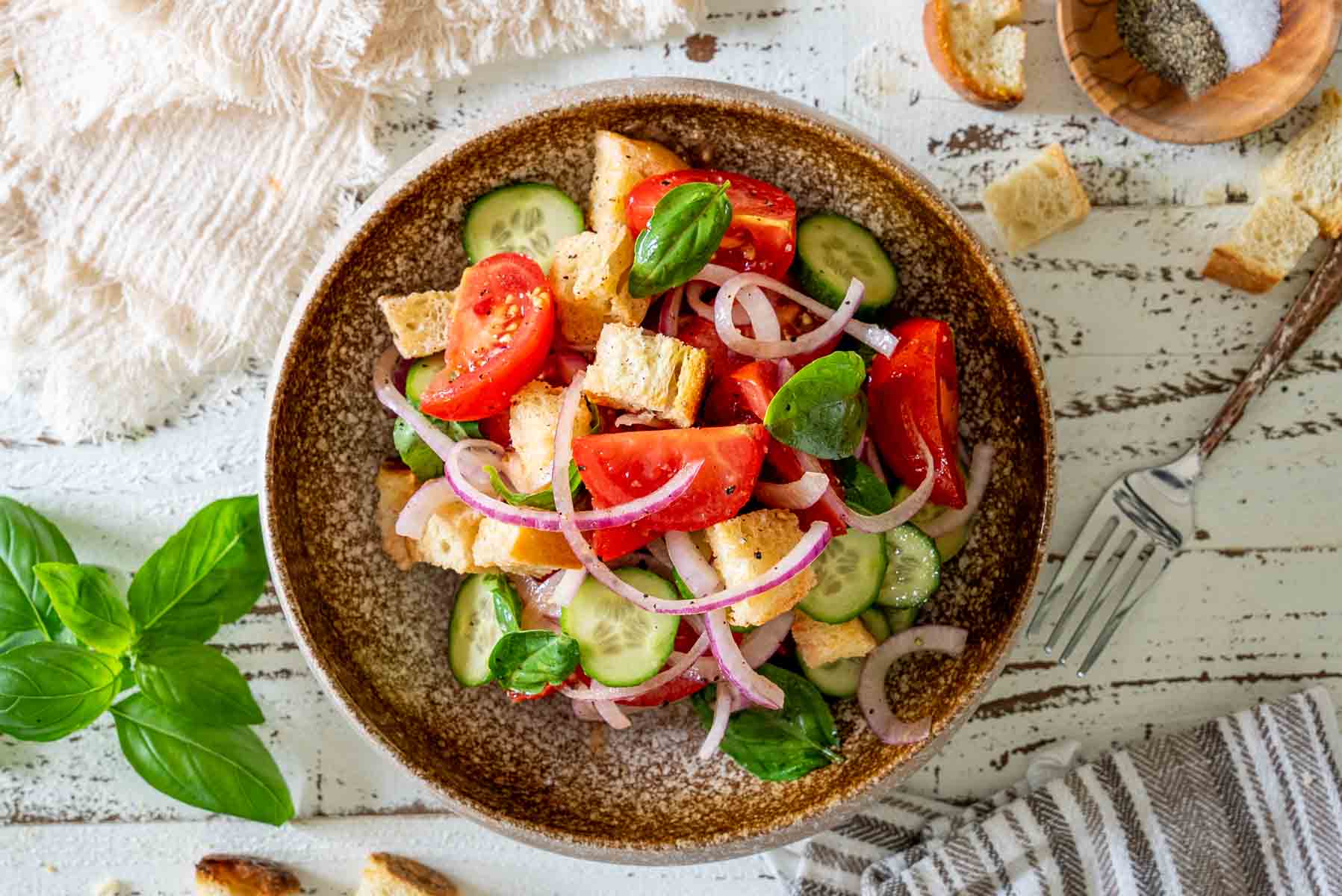 Salată Panzanella cu roșii, castraveți, ceapă roșie, pâine și busuioc, fotografiată de sus într-un bol maro.